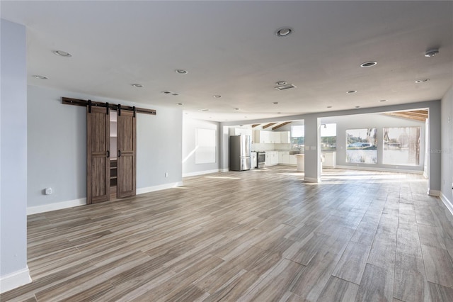 unfurnished living room with a barn door and light hardwood / wood-style flooring