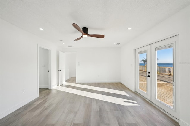 empty room with french doors, a water view, a textured ceiling, light hardwood / wood-style flooring, and ceiling fan