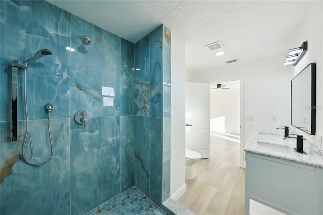 bathroom featuring vanity, hardwood / wood-style flooring, toilet, and tiled shower