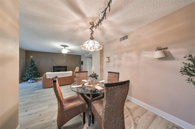 dining space with a textured ceiling, a notable chandelier, and light wood-type flooring