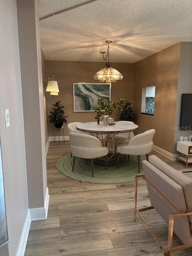 dining area featuring baseboards, wood finished floors, a textured ceiling, and an inviting chandelier