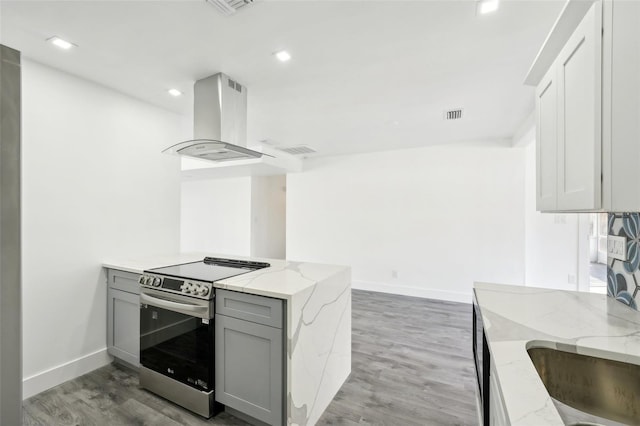 kitchen featuring electric range, light stone countertops, island exhaust hood, light hardwood / wood-style floors, and gray cabinets