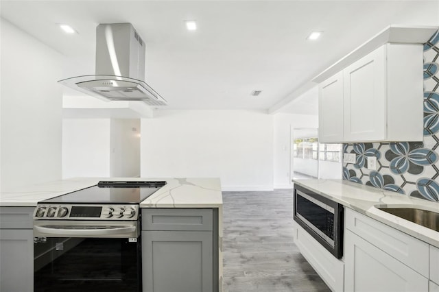 kitchen with appliances with stainless steel finishes, light wood-type flooring, light stone counters, wall chimney range hood, and white cabinets