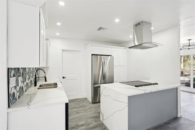 kitchen featuring sink, stainless steel fridge, island range hood, light stone counters, and white cabinetry