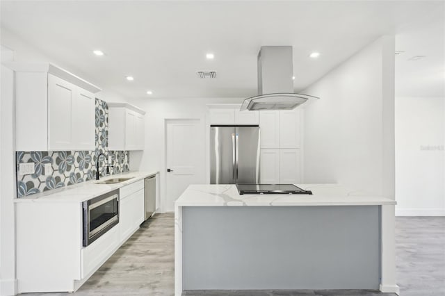 kitchen with light stone counters, stainless steel appliances, island range hood, sink, and white cabinetry