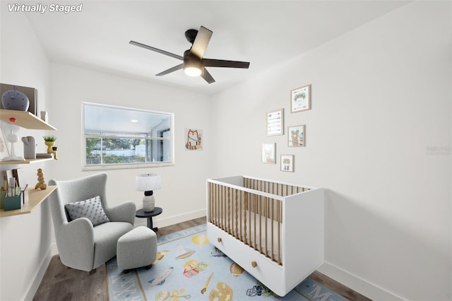 bedroom with ceiling fan, hardwood / wood-style floors, and a crib