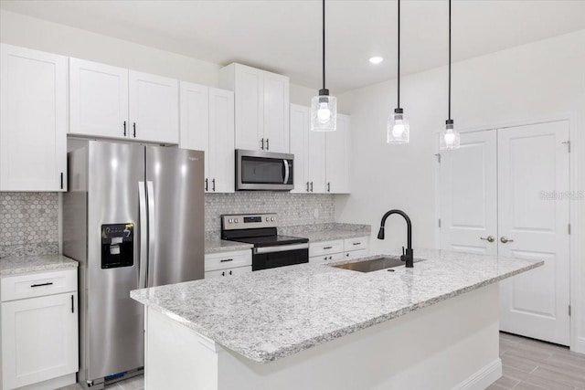 kitchen with a kitchen island with sink, sink, light stone countertops, appliances with stainless steel finishes, and white cabinetry