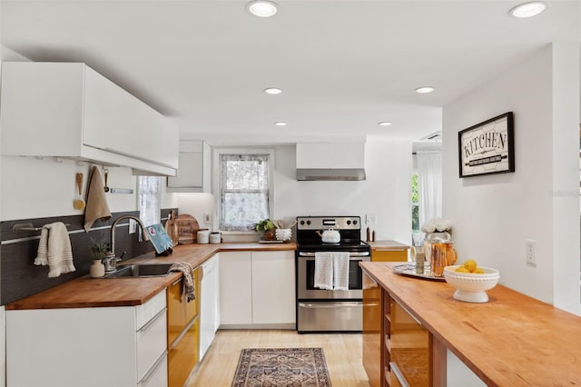 kitchen with stainless steel electric range oven, sink, wall chimney range hood, wood counters, and white cabinets