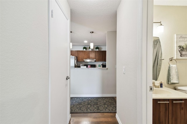 hallway with a textured ceiling, sink, and dark wood-type flooring