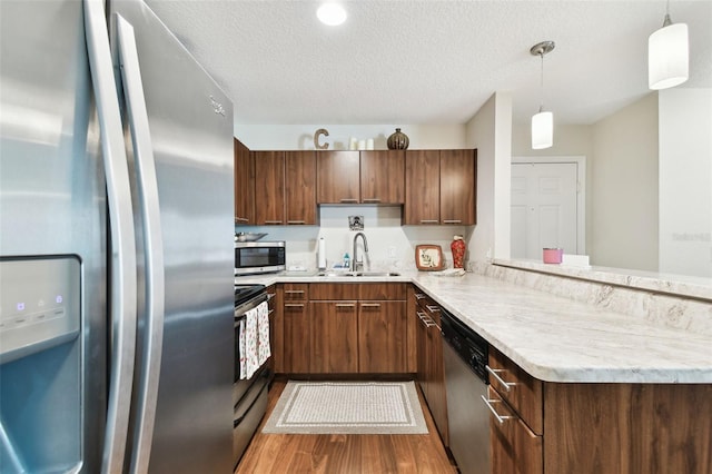 kitchen with pendant lighting, sink, light hardwood / wood-style floors, kitchen peninsula, and stainless steel appliances