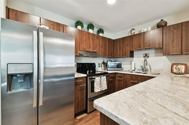 kitchen with a textured ceiling, light wood-type flooring, sink, and appliances with stainless steel finishes