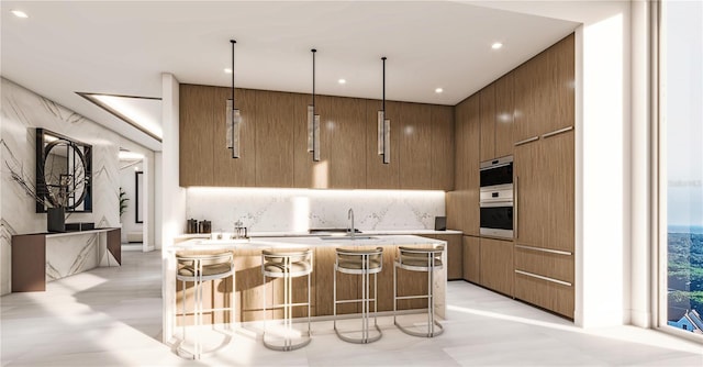 kitchen featuring a kitchen breakfast bar, sink, pendant lighting, and multiple ovens