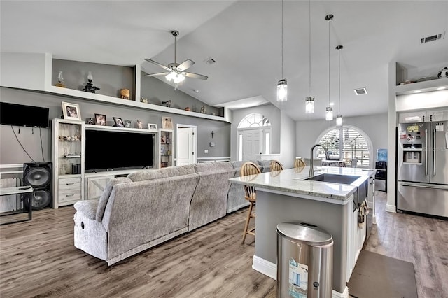 kitchen featuring white cabinets, hanging light fixtures, an island with sink, a kitchen bar, and stainless steel fridge with ice dispenser