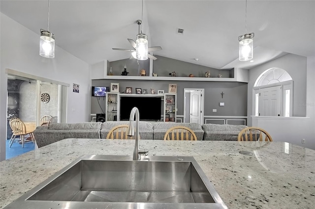 kitchen featuring light stone counters, sink, hanging light fixtures, and vaulted ceiling