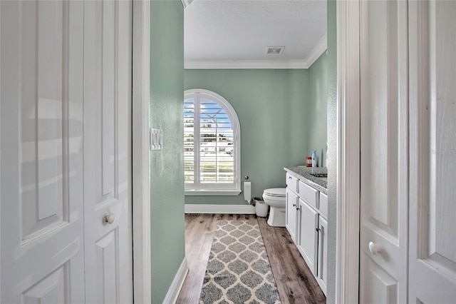 bathroom featuring crown molding, vanity, wood-type flooring, and toilet