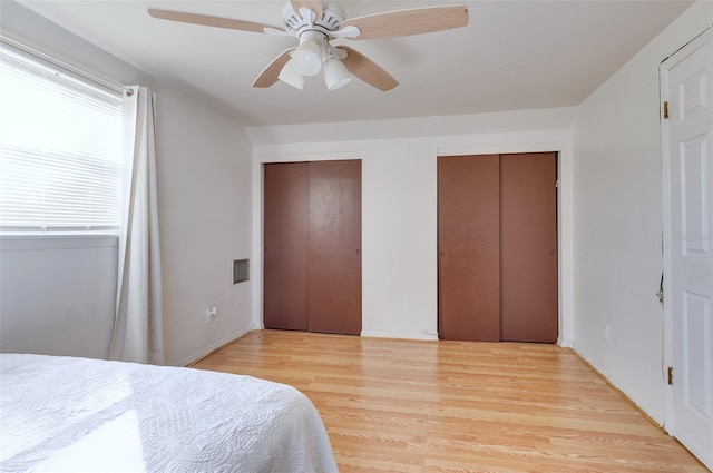 bedroom with light wood-type flooring, two closets, and ceiling fan