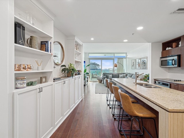 kitchen with sink, white cabinetry, light stone counters, an island with sink, and a breakfast bar