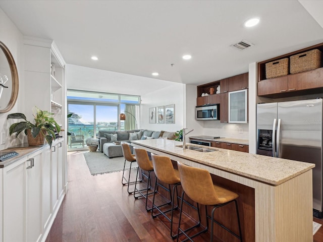 kitchen with a kitchen breakfast bar, a center island with sink, appliances with stainless steel finishes, dark hardwood / wood-style flooring, and sink