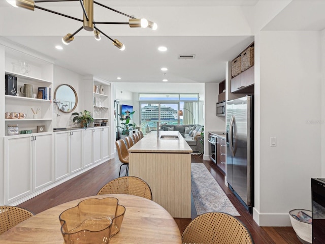 kitchen featuring dark wood-type flooring, a center island with sink, a notable chandelier, white cabinets, and appliances with stainless steel finishes