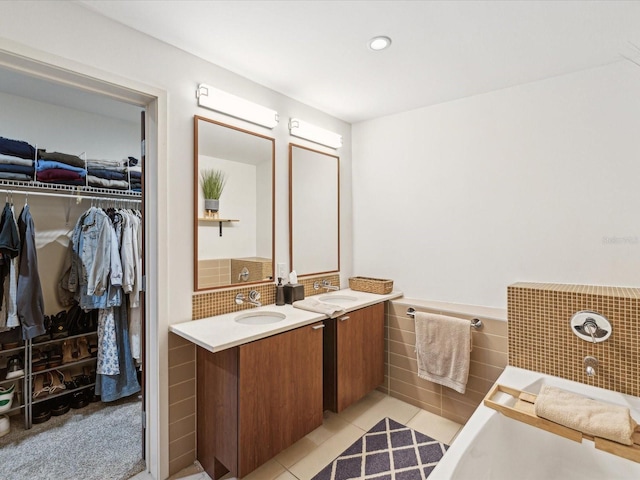 bathroom with tile walls, tile patterned flooring, a washtub, and vanity