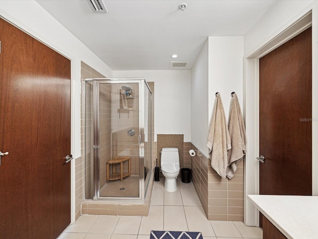 bathroom featuring toilet, tile patterned floors, tile walls, and a shower with door