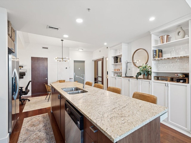 kitchen with appliances with stainless steel finishes, an island with sink, light stone countertops, dark hardwood / wood-style floors, and sink