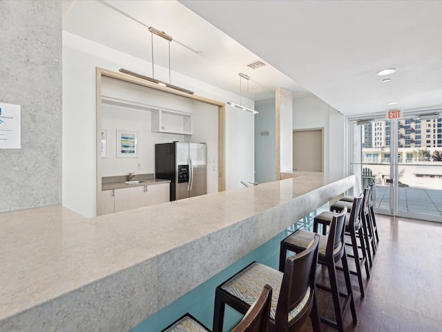 kitchen featuring a wall of windows, stainless steel refrigerator with ice dispenser, sink, white cabinetry, and decorative light fixtures