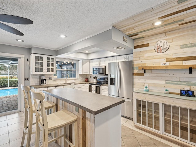 kitchen with appliances with stainless steel finishes, white cabinetry, wooden walls, a kitchen breakfast bar, and light tile patterned floors