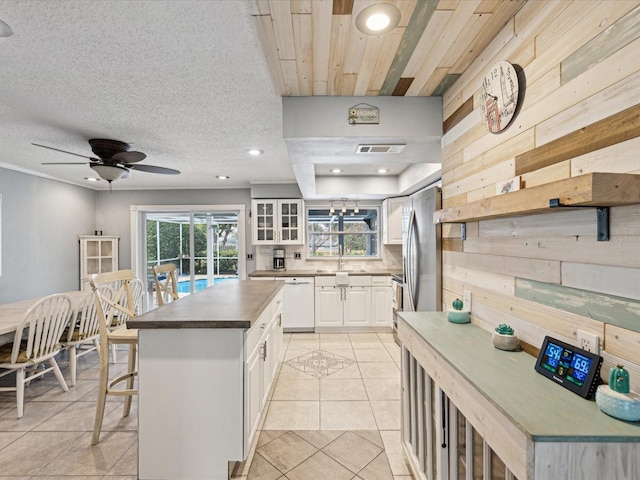 kitchen featuring white cabinetry, wood walls, light tile patterned flooring, white dishwasher, and a breakfast bar