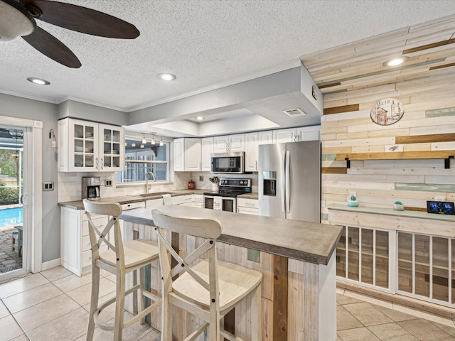 kitchen featuring white cabinetry, light tile patterned floors, a center island, wooden walls, and stainless steel appliances