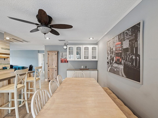 dining area featuring ceiling fan, crown molding, light tile patterned floors, and a textured ceiling