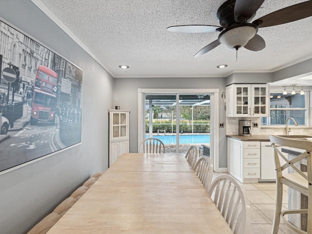 tiled dining space with sink, a textured ceiling, ceiling fan, and crown molding