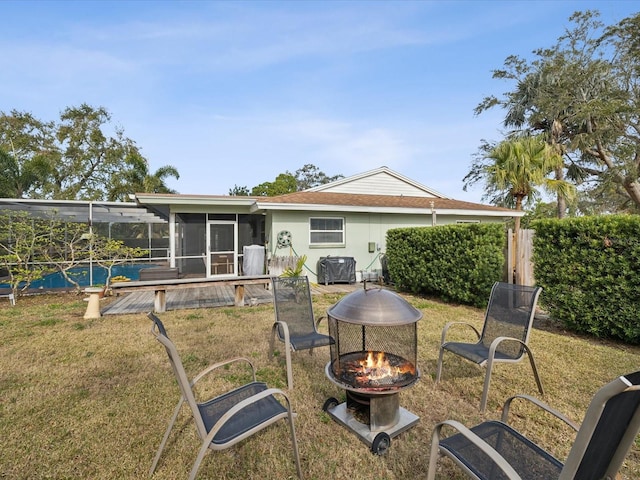 rear view of house with a sunroom, a fire pit, and a lawn