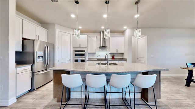 kitchen with a center island with sink, white cabinets, sink, appliances with stainless steel finishes, and decorative light fixtures