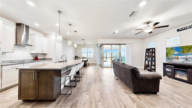 kitchen with white cabinets, pendant lighting, a center island with sink, and wall chimney range hood