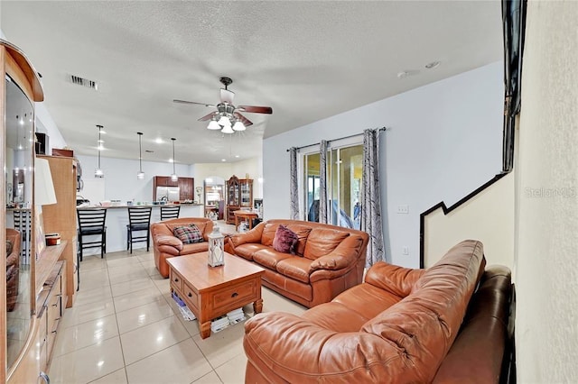 living room with ceiling fan, light tile patterned floors, and a textured ceiling