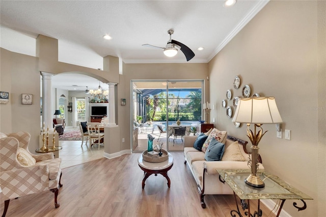 living room featuring hardwood / wood-style floors, ceiling fan with notable chandelier, ornate columns, and ornamental molding