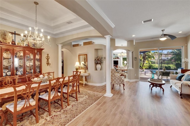 dining space featuring ceiling fan with notable chandelier, a raised ceiling, crown molding, light hardwood / wood-style floors, and decorative columns