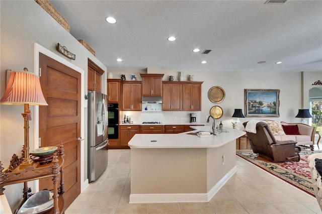 kitchen with sink, stainless steel appliances, a textured ceiling, a kitchen island with sink, and light tile patterned floors