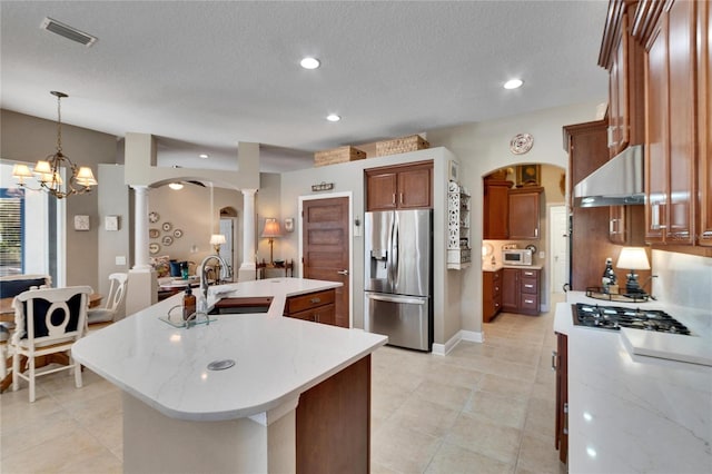 kitchen featuring decorative columns, stainless steel appliances, sink, an inviting chandelier, and an island with sink