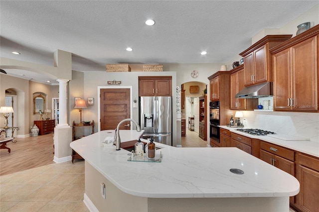 kitchen featuring sink, ornate columns, an island with sink, tasteful backsplash, and stainless steel appliances