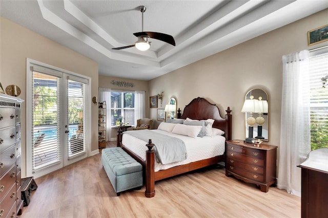 bedroom with ceiling fan, french doors, a raised ceiling, light hardwood / wood-style flooring, and access to outside