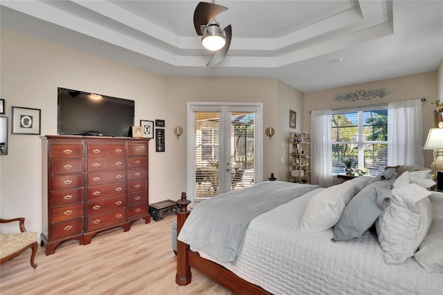 bedroom featuring access to exterior, light hardwood / wood-style floors, a raised ceiling, and ceiling fan