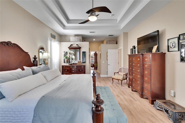 bedroom with a tray ceiling, ceiling fan, and light wood-type flooring