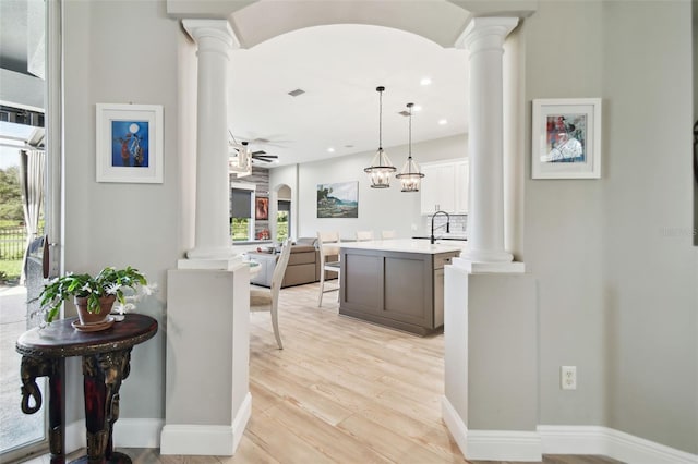 kitchen with ceiling fan with notable chandelier, hanging light fixtures, light hardwood / wood-style flooring, an island with sink, and white cabinetry