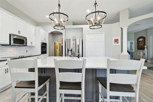 kitchen featuring a center island, hanging light fixtures, stainless steel appliances, decorative columns, and backsplash