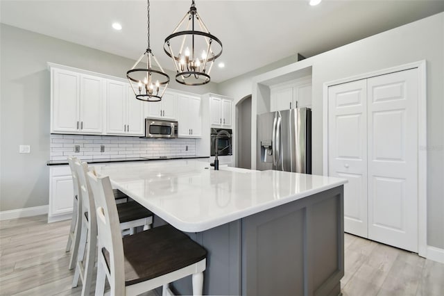 kitchen with a center island with sink, pendant lighting, white cabinets, and appliances with stainless steel finishes