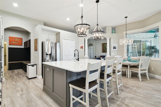 kitchen with light wood-type flooring, ornate columns, pendant lighting, a center island with sink, and white cabinets