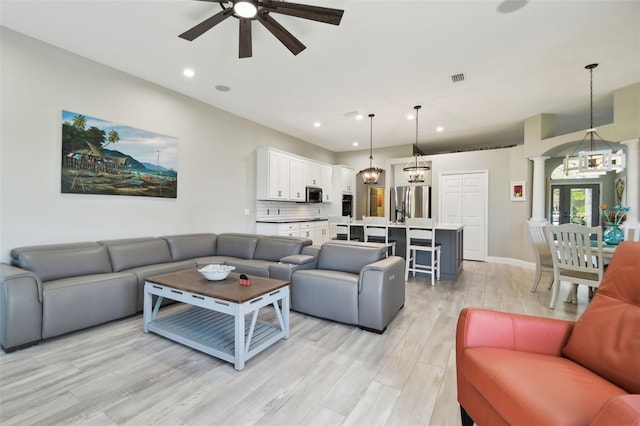 living room featuring decorative columns, light hardwood / wood-style flooring, and ceiling fan with notable chandelier