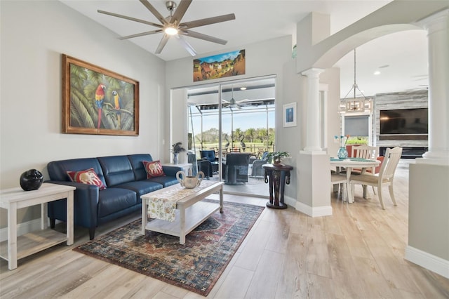 living room featuring decorative columns, light hardwood / wood-style floors, and ceiling fan with notable chandelier